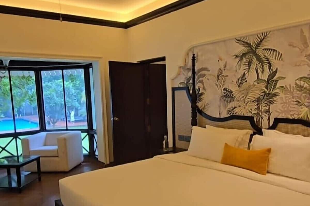 Une chambre moderne avec un grand lit, un ventilateur de plafond et une vue sur une piscine, visible à travers de grandes fenêtres.