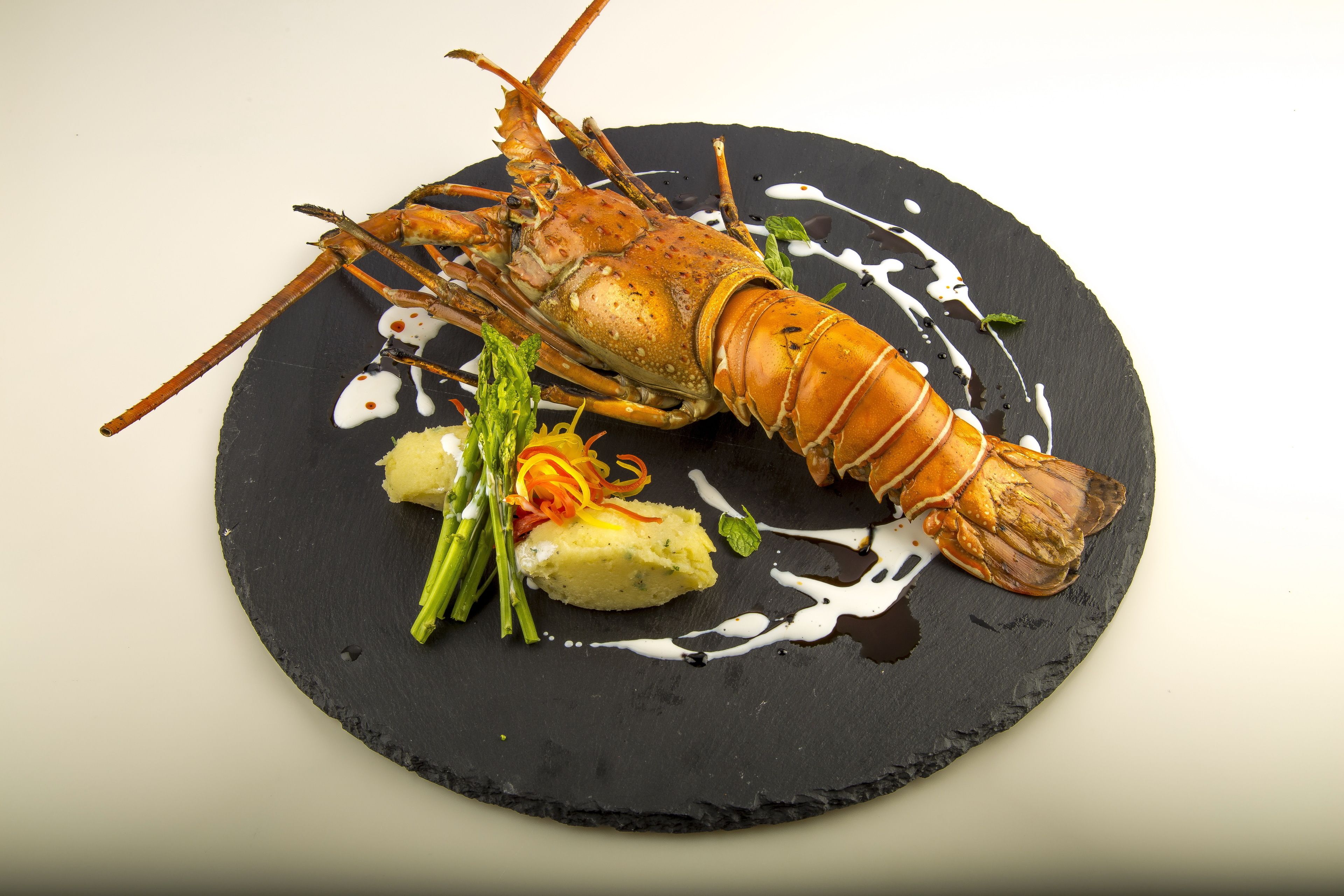 Un plato de langosta sobre una fuente negra, con espárragos verdes y un acompañamiento de verdura amarilla.