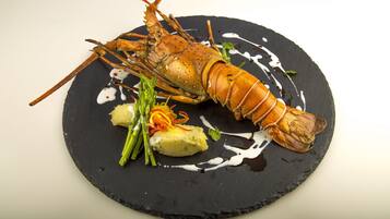Un plato de langosta sobre una fuente negra, con espárragos verdes y un acompañamiento de verdura amarilla.