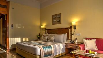 A hotel room with a large bed, a red sofa, a glass coffee table with fruits, and two bedside lamps.