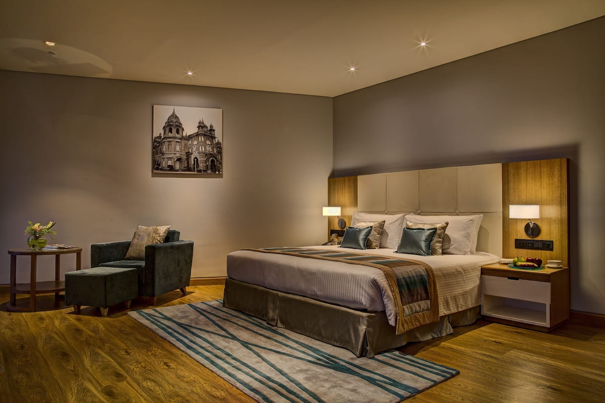 A modern bedroom with a large bed, a nightstand, a chair, and a framed picture on the wall.