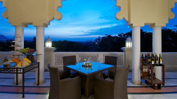 Un área de comedor al aire libre con una mesa preparada para dos personas, rodeada de sillas de mimbre, bajo un arco decorativo.