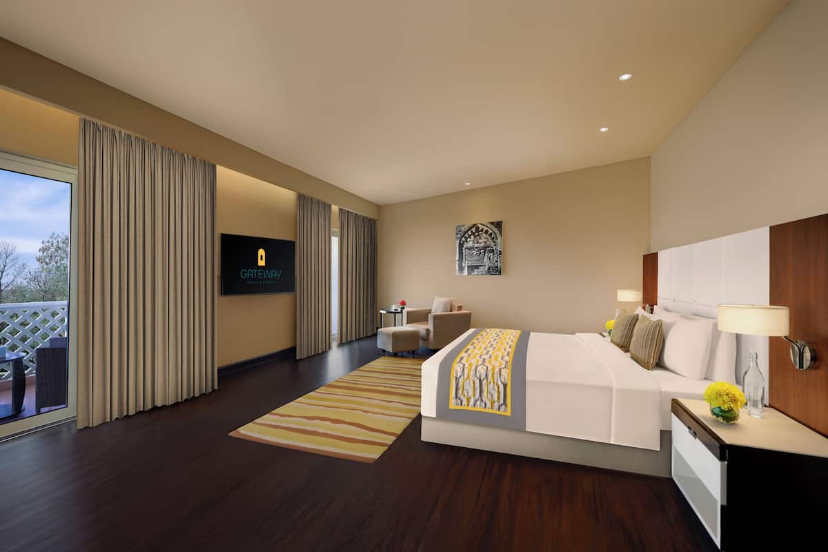 A modern hotel room with a large bed, a TV, a desk with a lamp, and a view of the outdoors.