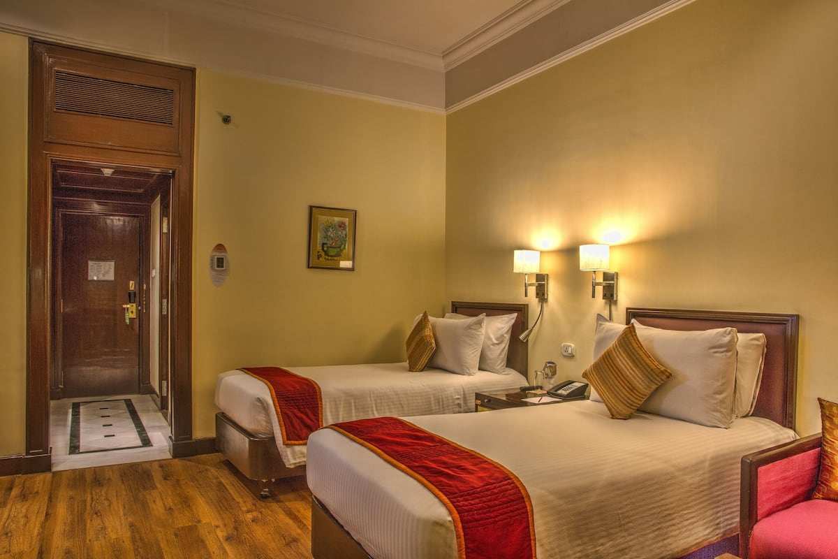 A hotel room with two beds, a wooden door, a wall-mounted light, and a small painting.