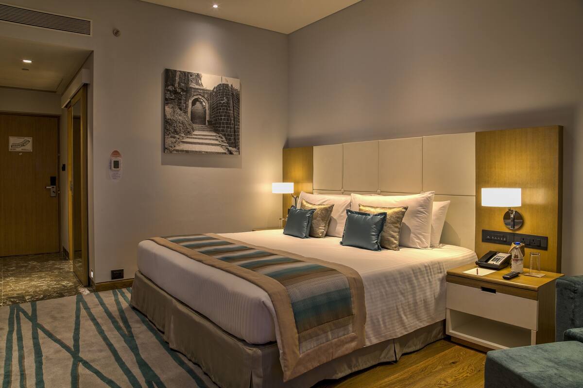 A hotel room with a large bed, bedside tables, a wall-mounted phone, and a framed picture.