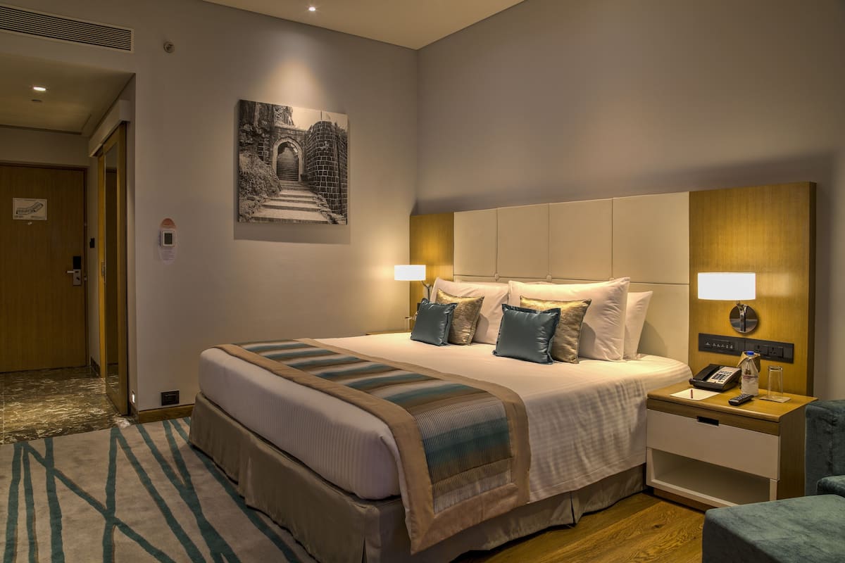 A hotel room with a large bed, bedside tables, a nightstand, a wall-mounted phone, a lamp, and a framed picture on the wall.