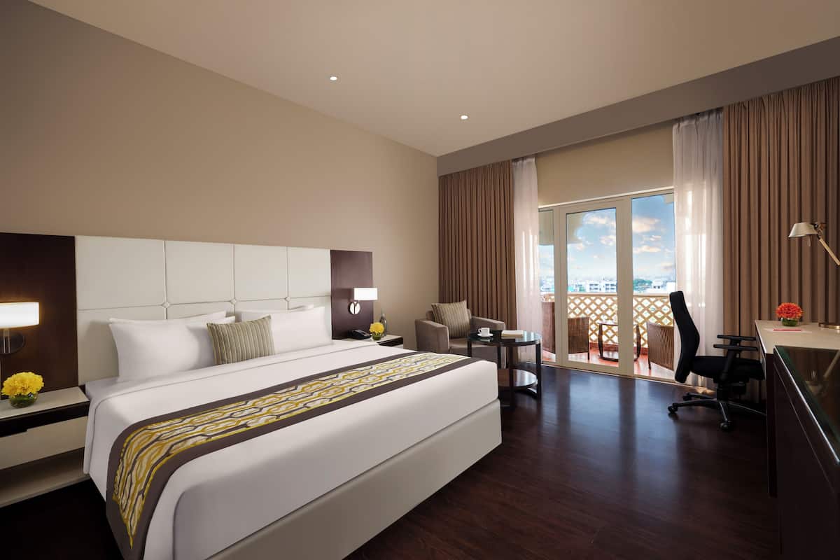 A hotel room with a large bed, a desk, a chair, a small table, and a balcony with a view.