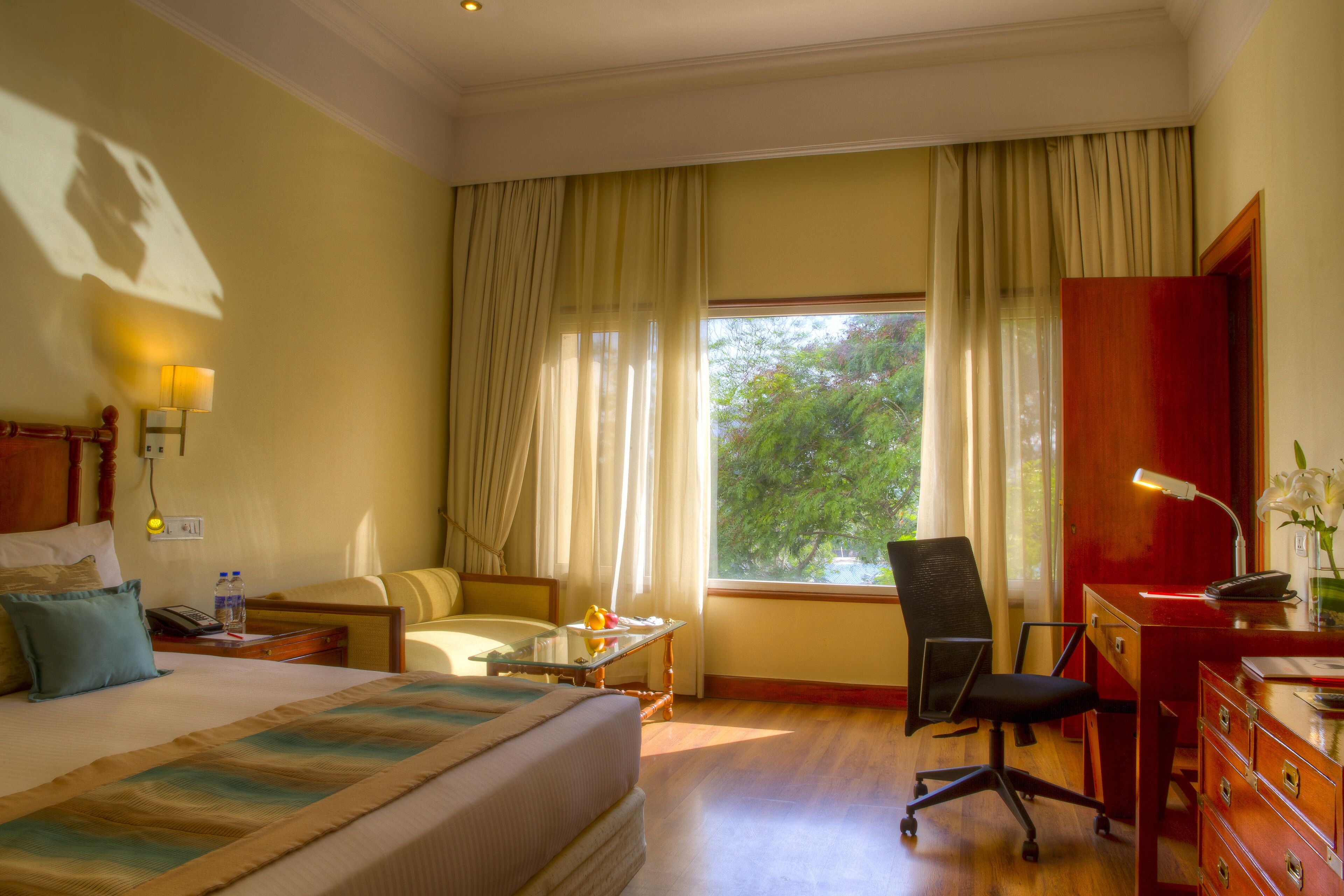 Une chambre d’hôtel avec un lit, un bureau, une chaise, une petite table et une fenêtre avec des rideaux.