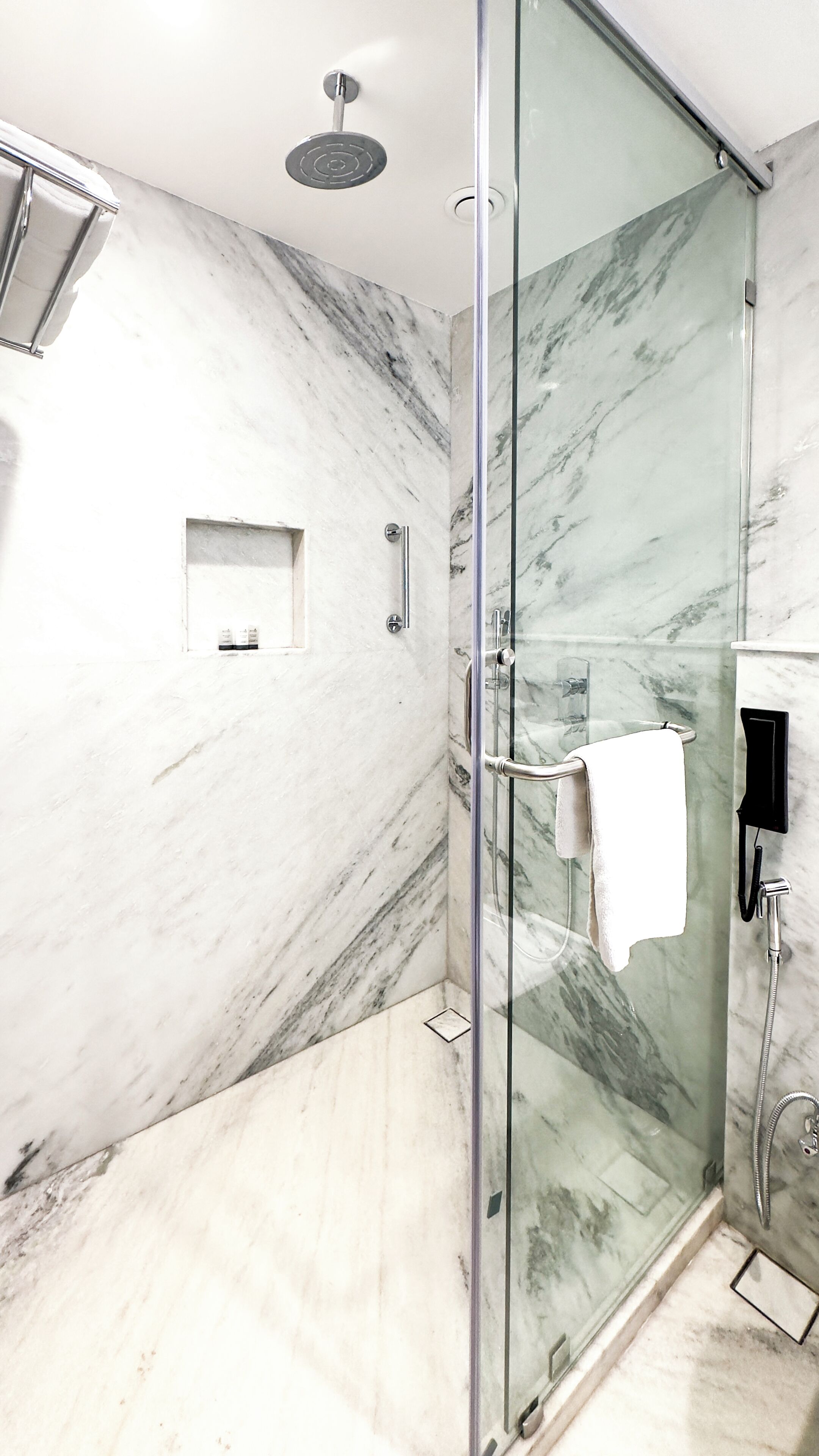 A modern bathroom with a glass-enclosed shower, marble walls, and a towel rack.