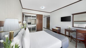 Una habitación de hotel con cama, escritorio, silla, televisor y armario.