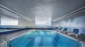 Una piscina interior con agua azul cristalina, suelo de baldosas y sillones de descanso a los lados.
