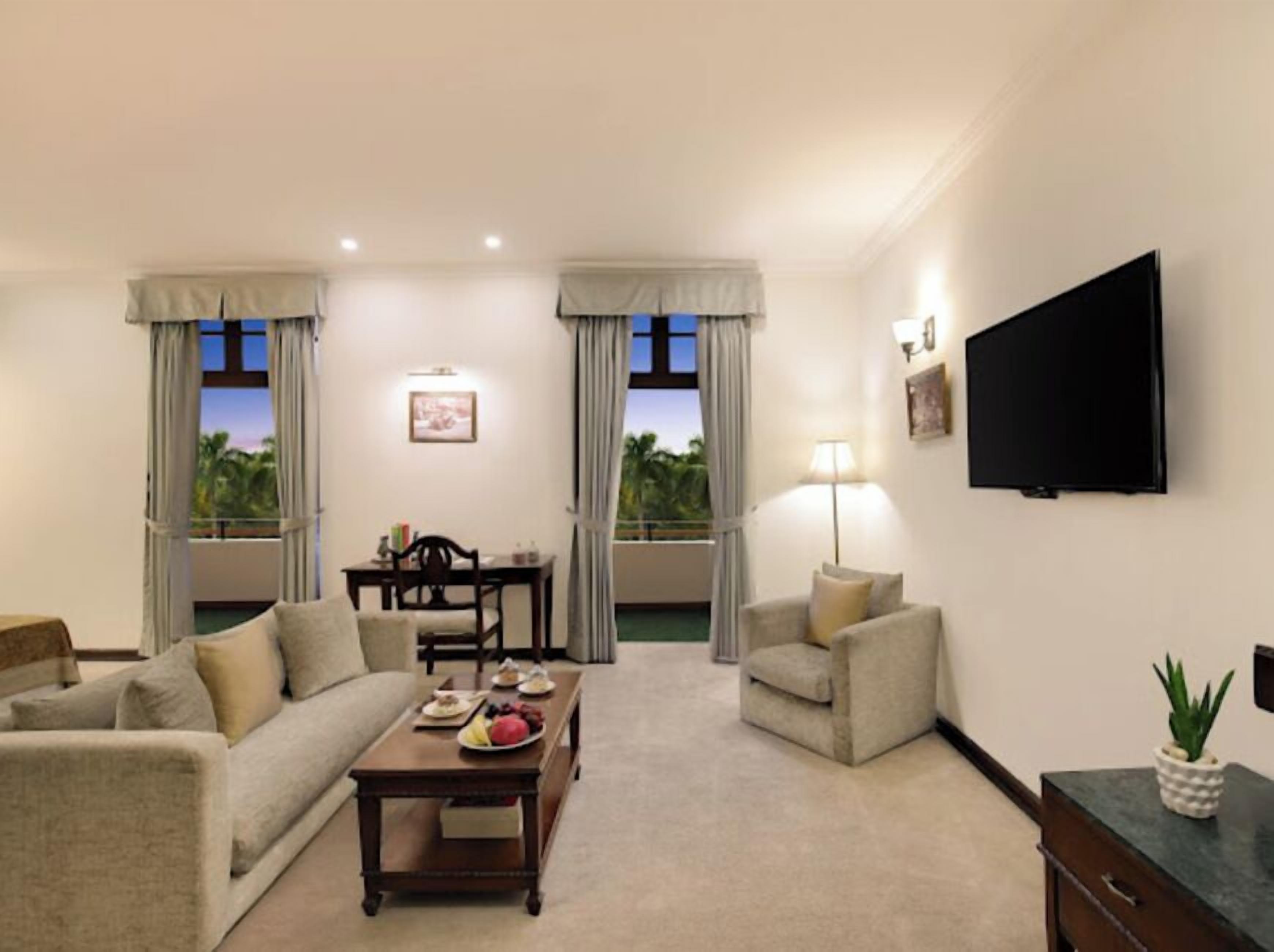 Une chambre d’hôtel équipée d’un canapé, d’un fauteuil, d’une table à manger et d’un téléviseur fixé au mur.