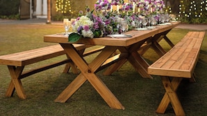 A wooden picnic table set up outdoors with floral centerpieces and glasses. - Ambassador, New Delhi - IHCL SeleQtions (New Delhi)
