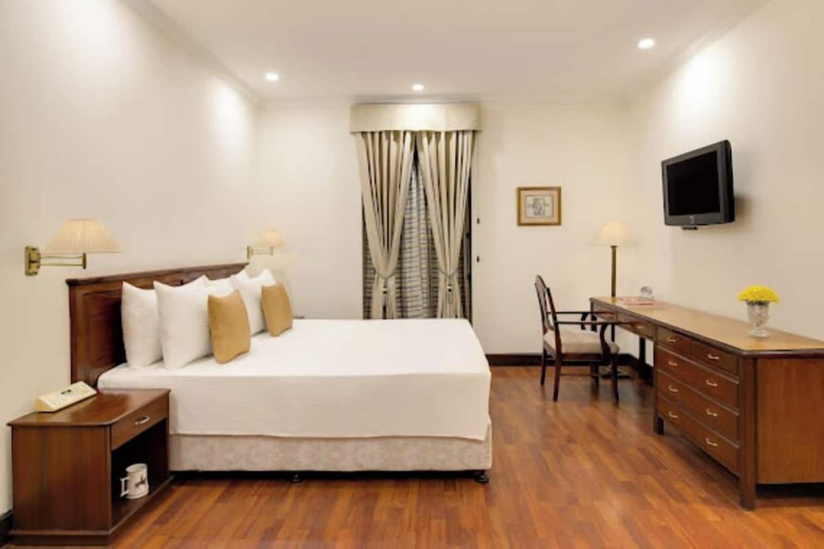 A hotel room with a bed, bedside tables, a desk, a chair, a television, and a window with curtains.