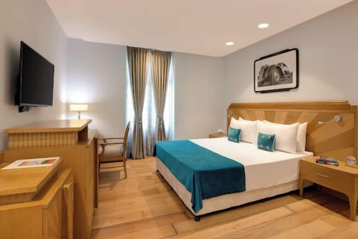A hotel room with a bed, a desk, a chair, a television, and a window with curtains.