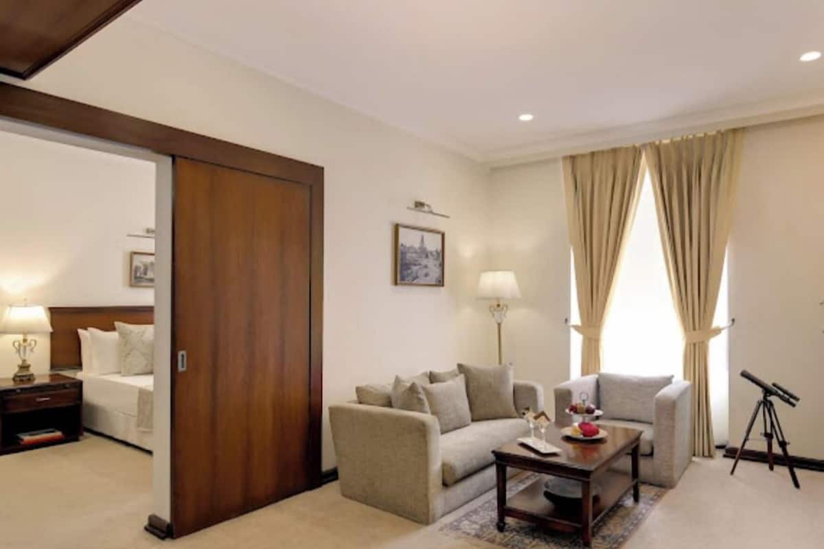 A hotel room with a bed, a sofa, a coffee table, a lamp, a picture on the wall, and a telescope.