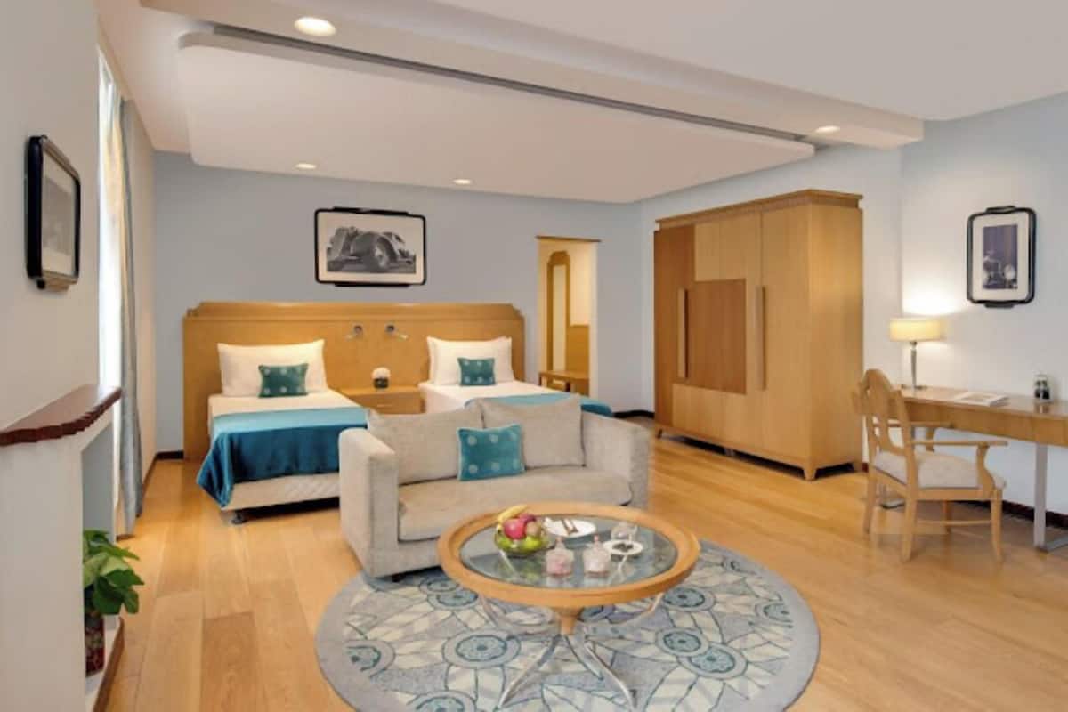 A hotel room with a bed, a sofa, a round coffee table, a desk with a chair, and a wardrobe.