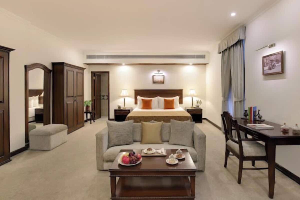 A hotel room with a bed, a sofa, a coffee table with fruit, a desk, and a chair.