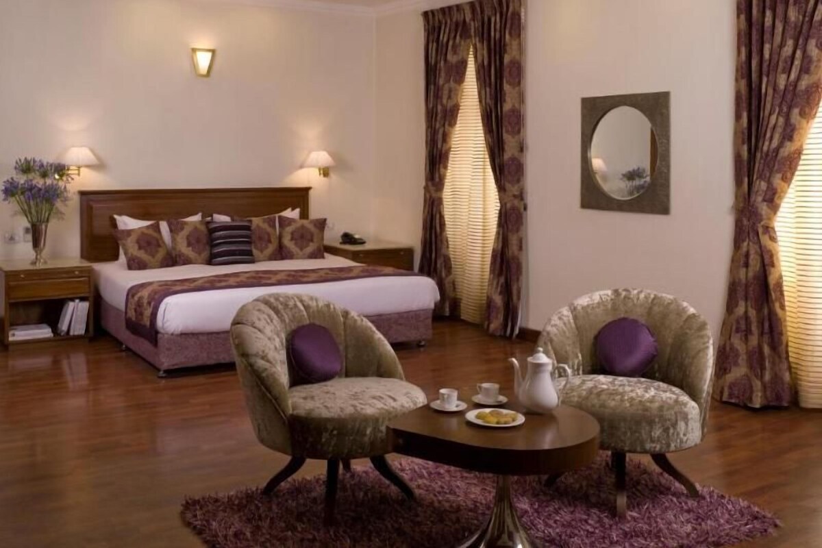 A hotel room with a bed, two armchairs, a round table with a teapot, and a mirror on the wall.