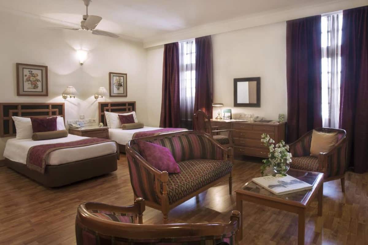 A hotel room with two beds, a desk, a chair, a coffee table, and a ceiling fan.