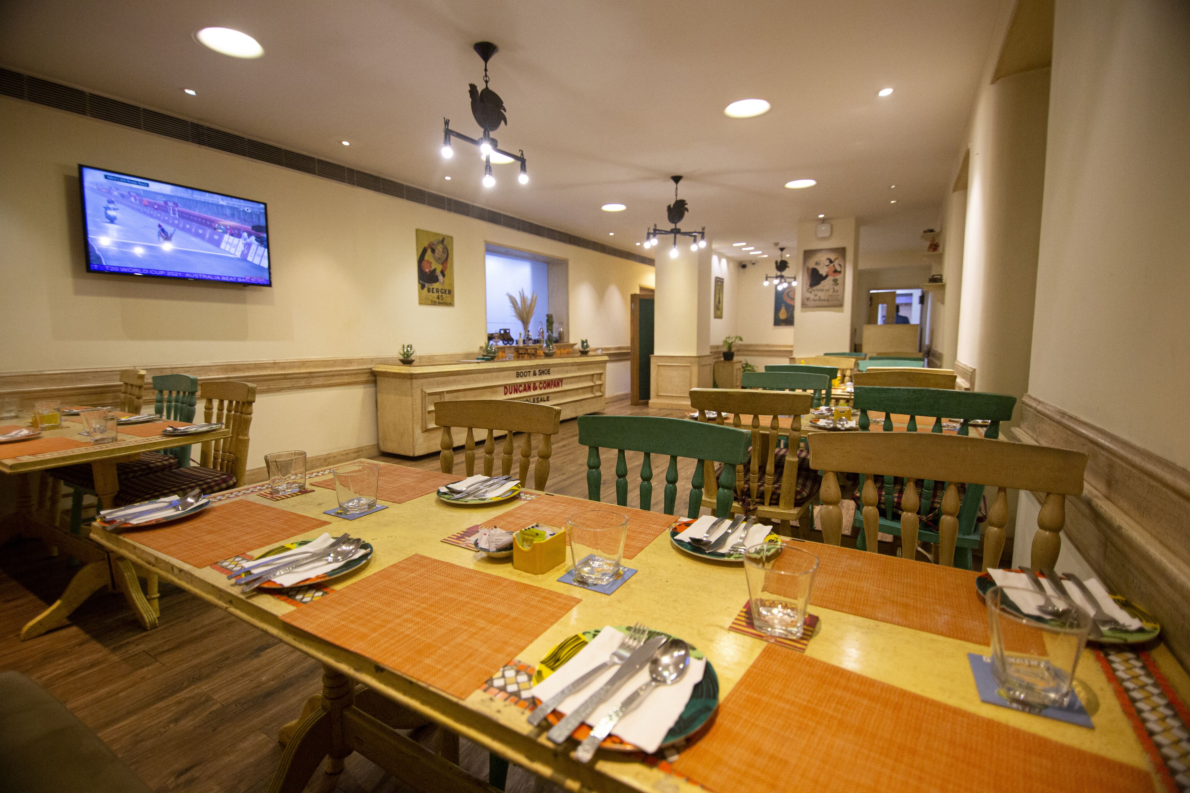 A restaurant with wooden tables and chairs, a television mounted on the wall, and a counter with a menu.