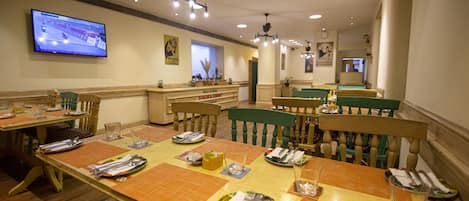 A restaurant with wooden tables and chairs, a television mounted on the wall, and a counter with a menu.