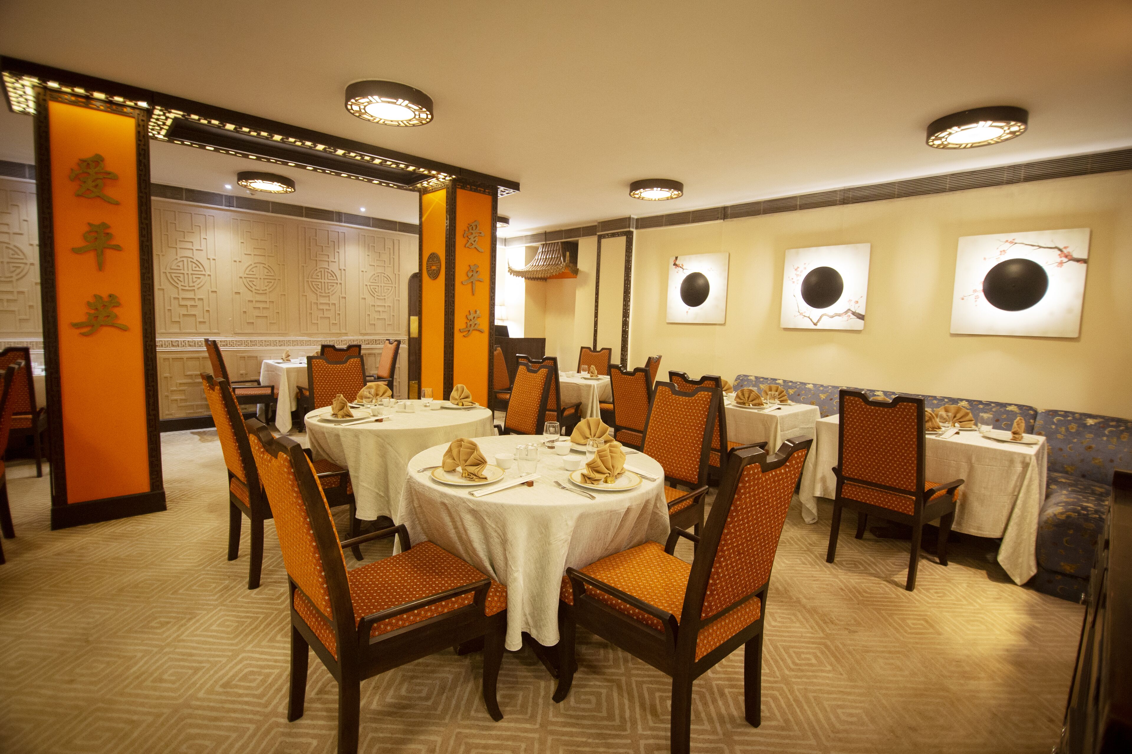 A restaurant with round tables, orange chairs, and traditional decor.