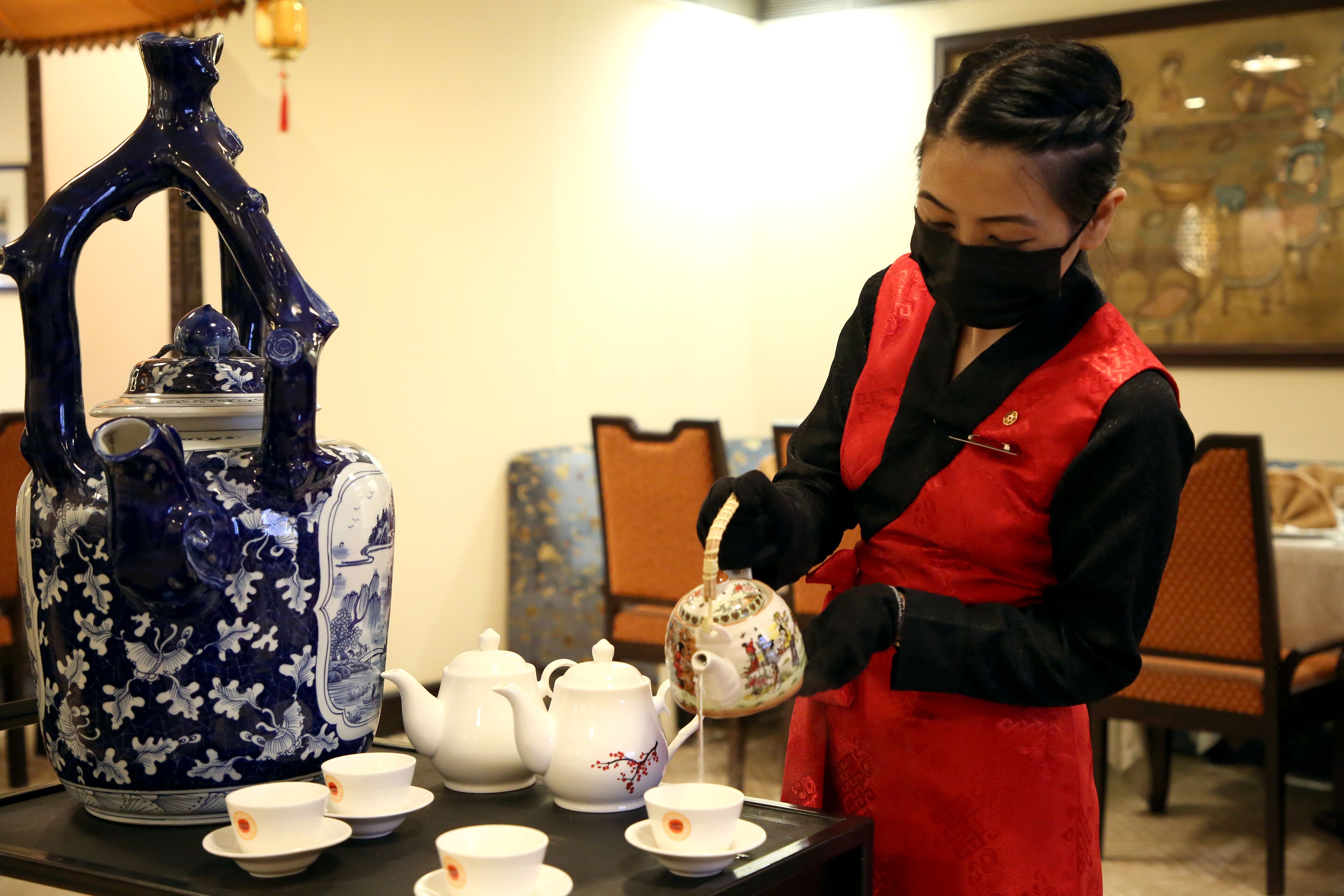 Une personne servant du thé avec une théière et des tasses bleues et blanches sur une table.