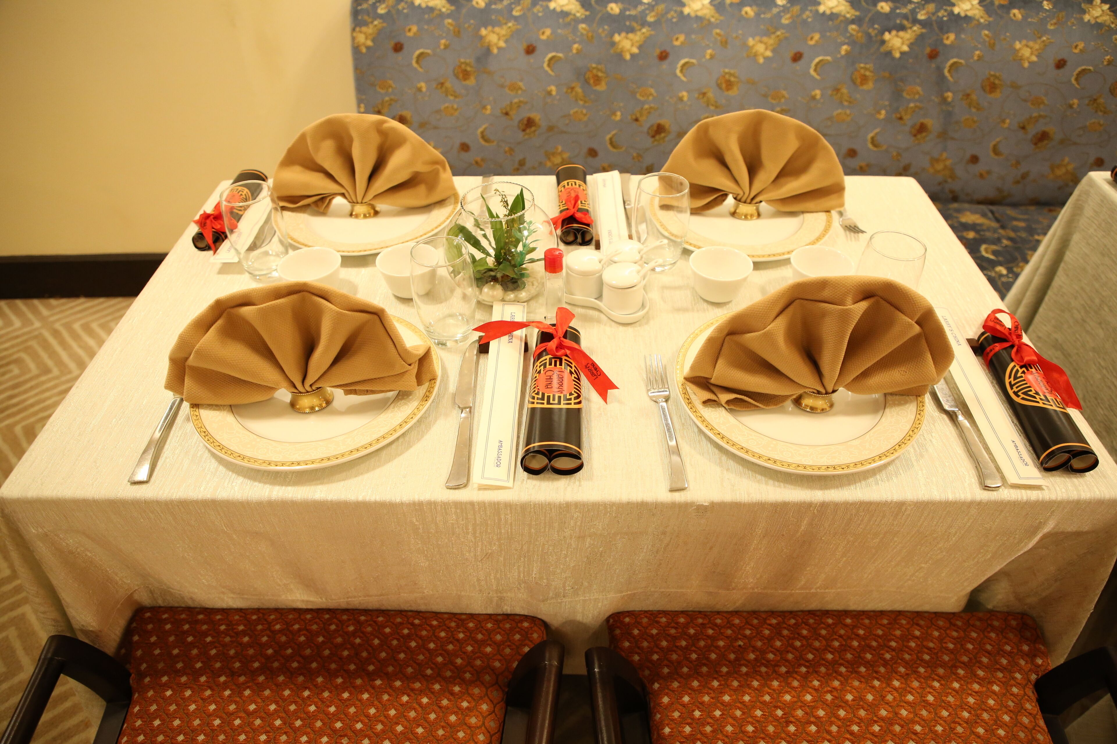 Une table à manger dressée avec des serviettes pliées, des couverts et une petite plante décorative.