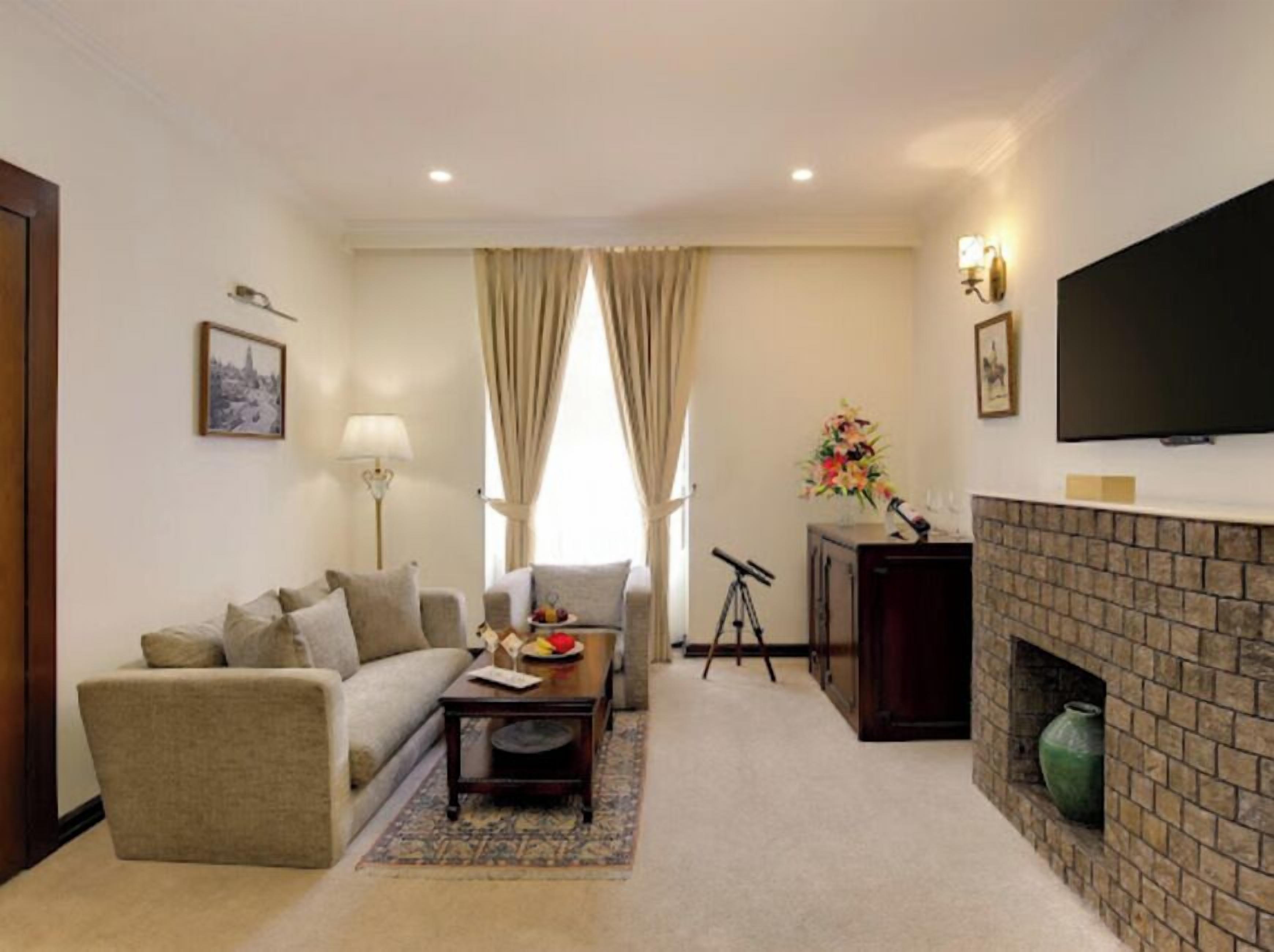 A living room with a sofa, coffee table, fireplace, television, and curtains.