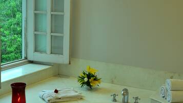 A bathroom with a bathtub filled with rose petals, a window with a view of greenery, and a vase with yellow flowers on the counter.