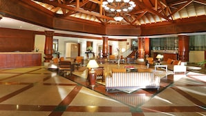 Un lobby espacioso con techo alto, vigas de madera, un candelabro central y una mesa de recepción.