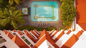 Vista aérea de un resort con piscina central, palmeras y un diseño de techo característico.