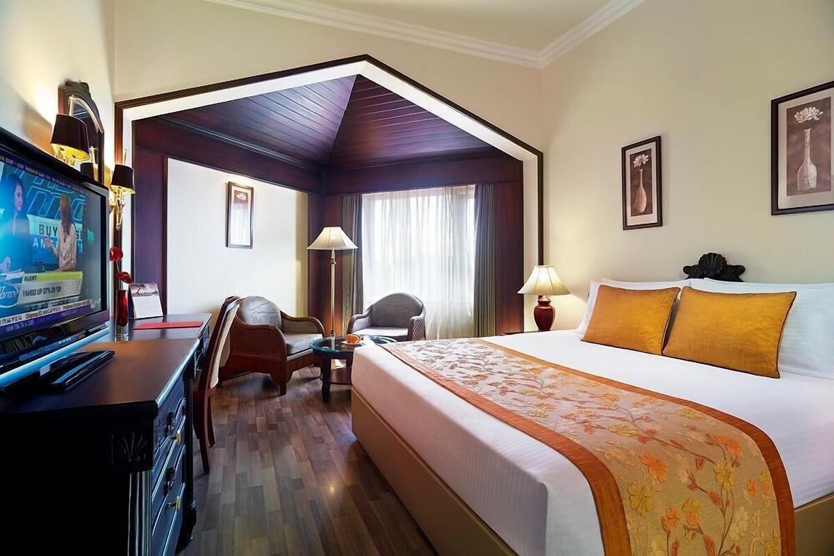 A hotel room with a large bed, a desk with a computer, a chair, a lamp, and a television.