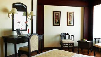 A hotel room with a bed, a desk, two chairs, a laptop, and two framed pictures on the wall.