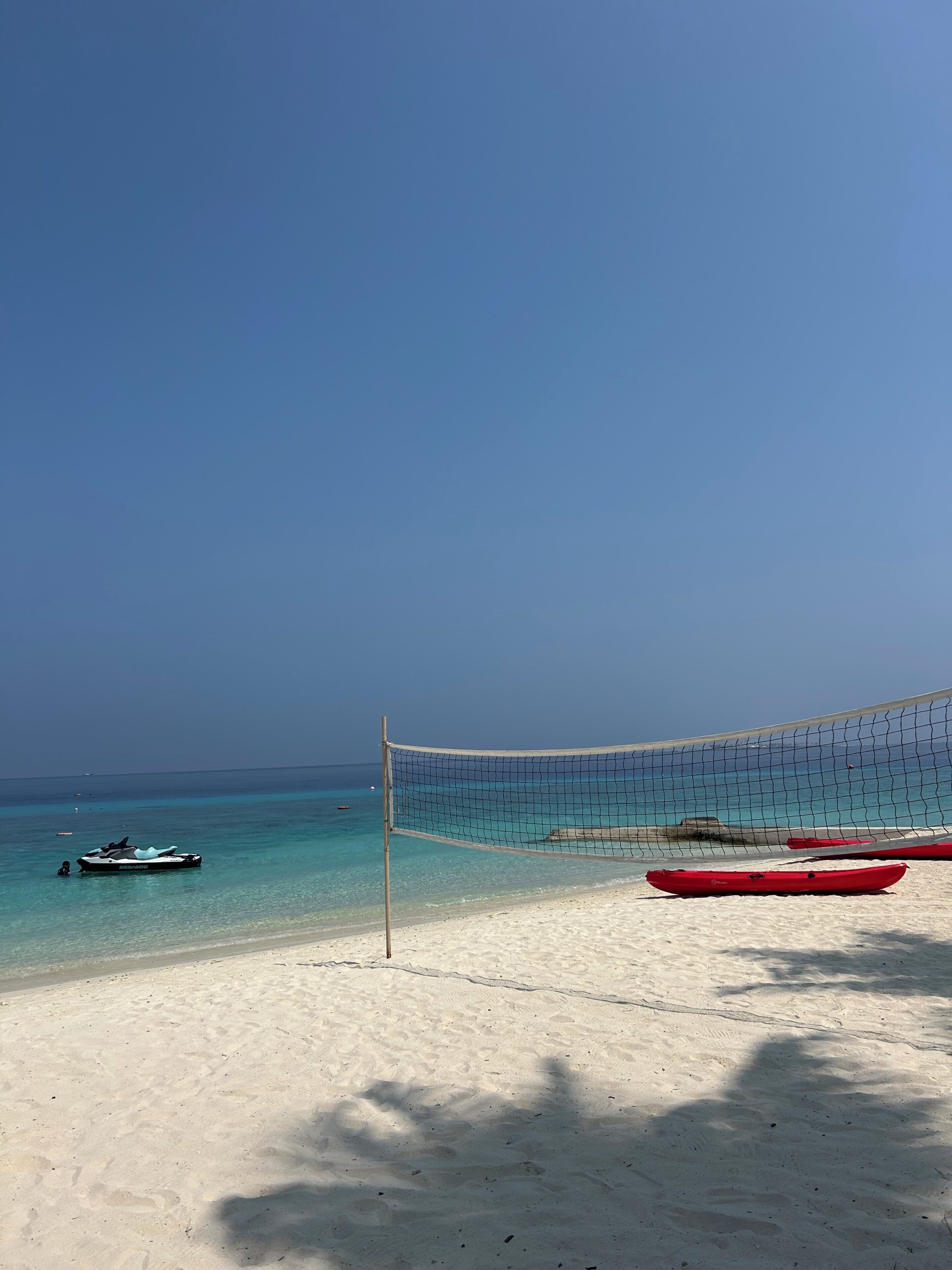 A beach with a volleyball net, a jet ski, and kayaks on the sand.