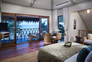 Ein Schlafzimmer mit einem großen Bett, einem Fernseher, einem Balkon mit Meerblick und einem Essbereich mit Korbmöbeln.