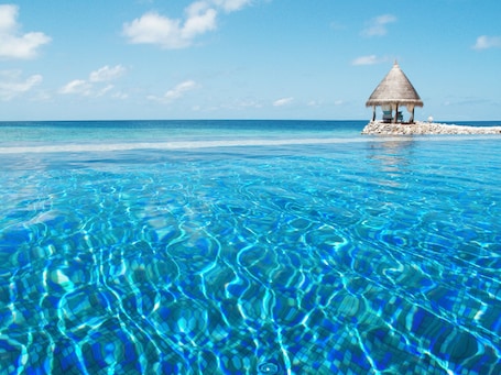 Una piscina al aire libre, sombrillas, sillones reclinables de piscina. Taj Coral Reef Resort & Spa Maldives – A Premium All Inclusive Resort