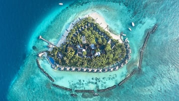 An aerial view of a tropical island resort with overwater bungalows, a central building, and a swimming pool.
