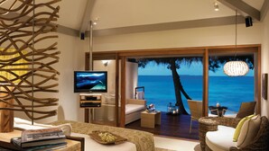 A bedroom with a large TV, a bed, a wicker sofa, and a view of the ocean. - Taj Coral Reef Resort & Spa Maldives – A Premium All Inclusive Resort (Hembadhu Island)