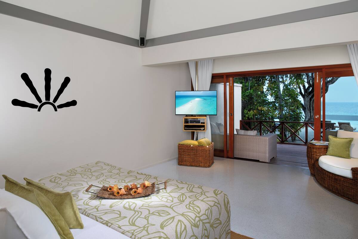 A hotel room with a bed, a television, a wicker sofa, and a balcony with a view of the sea.