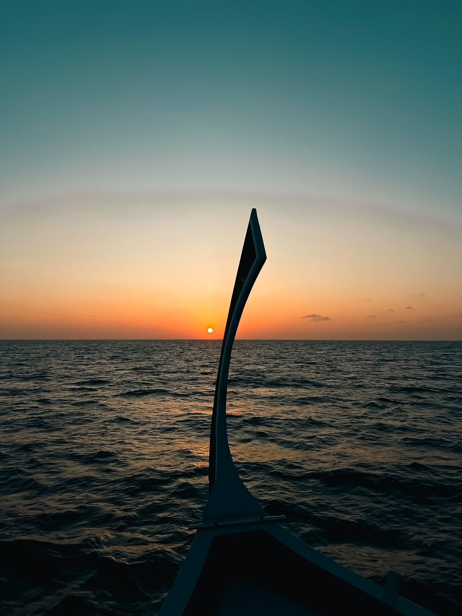 A sunset over the ocean with a boat's bow in the foreground.