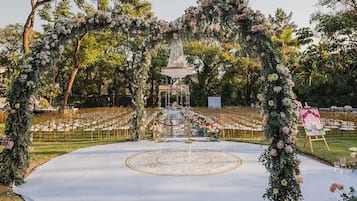 Un lugar para bodas al aire libre con un arco decorado, una fuente central y un piso de baile circular.