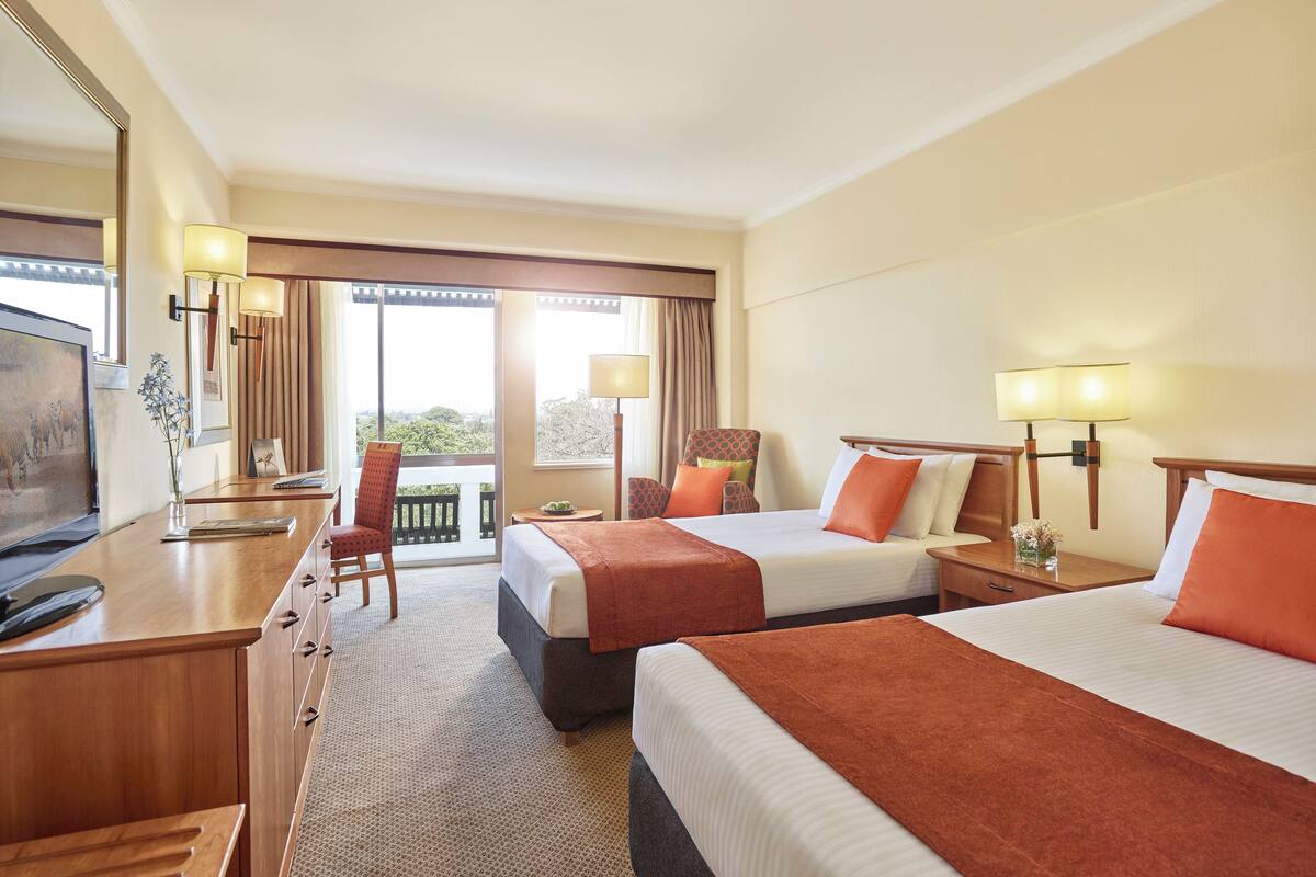 A hotel room with two beds, a desk, a chair, a TV, and a balcony with a view.