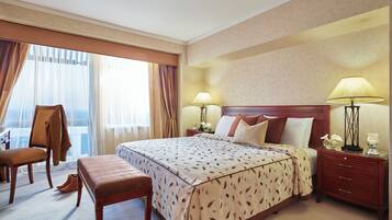 Una habitación de hotel con una cama grande, un banco de madera, una silla y una mesita de noche con lámparas.