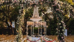 Eine Hochzeitslocation im Freien mit einem Blumenschmuckbogen, einem zentralen Pavillon und Reihen goldener Stühle.
