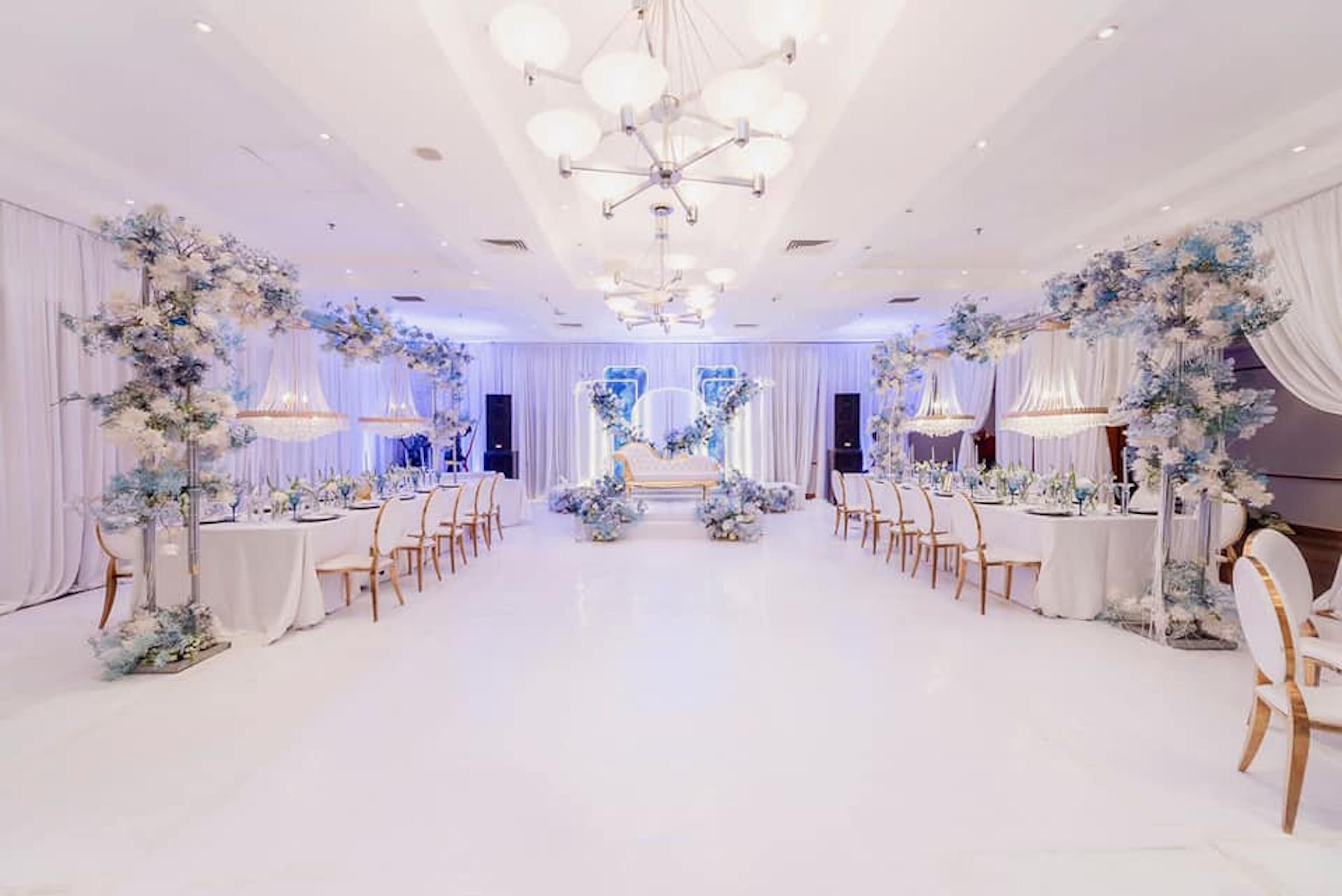 A banquet hall with white tables and chairs, floral centerpieces, and chandeliers.