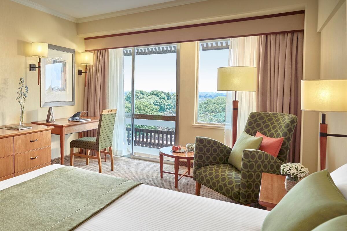 A hotel room with a bed, a desk, a chair, a table, and a view of the outdoors.