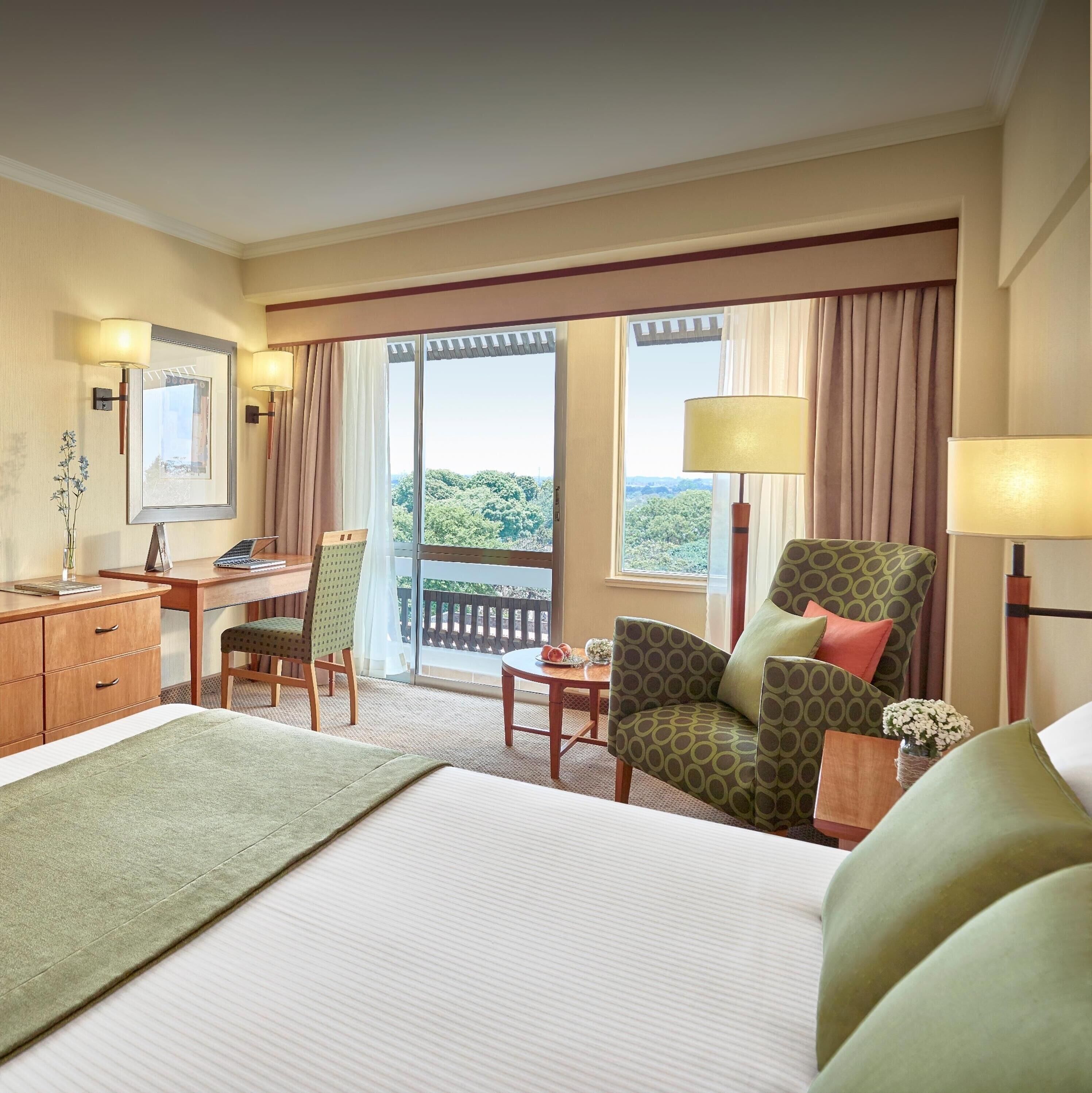 Ein Hotelzimmer mit Bett, Schreibtisch, Stuhl, Tisch und Blick ins Freie.