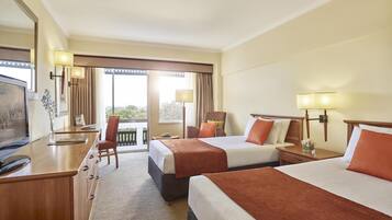 A hotel room with two beds, a desk, a TV, and a balcony with a view.